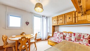 A cozy room with a wooden dining table and chairs, a sofa with patterned cushions, and wooden cabinets above the sofa.