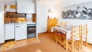 Eine kompakte Küche mit Herd, Backofen und Spüle, ein Esstisch mit Stühlen und ein Bergbild an der Wand.