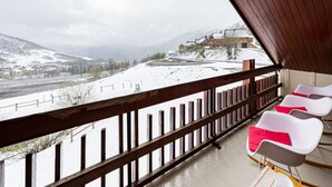 Ein Balkon mit Holzwerteln, der auf eine verschneite Landschaft mit Gebäuden und Bergen blickt.