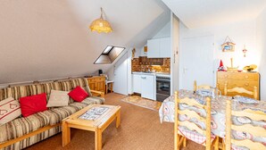 Ein gemütliches Wohnzimmer mit Sofa, Couchtisch und Esstisch. Im Hintergrund ist eine Küche mit Herd und Spüle zu sehen.