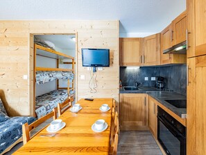 Pieni huone, jossa on kerrossänky, ruokapöytä astioineen, televisio sekä pieni keittiönurkkaus, jossa on liesi ja pesuallas.