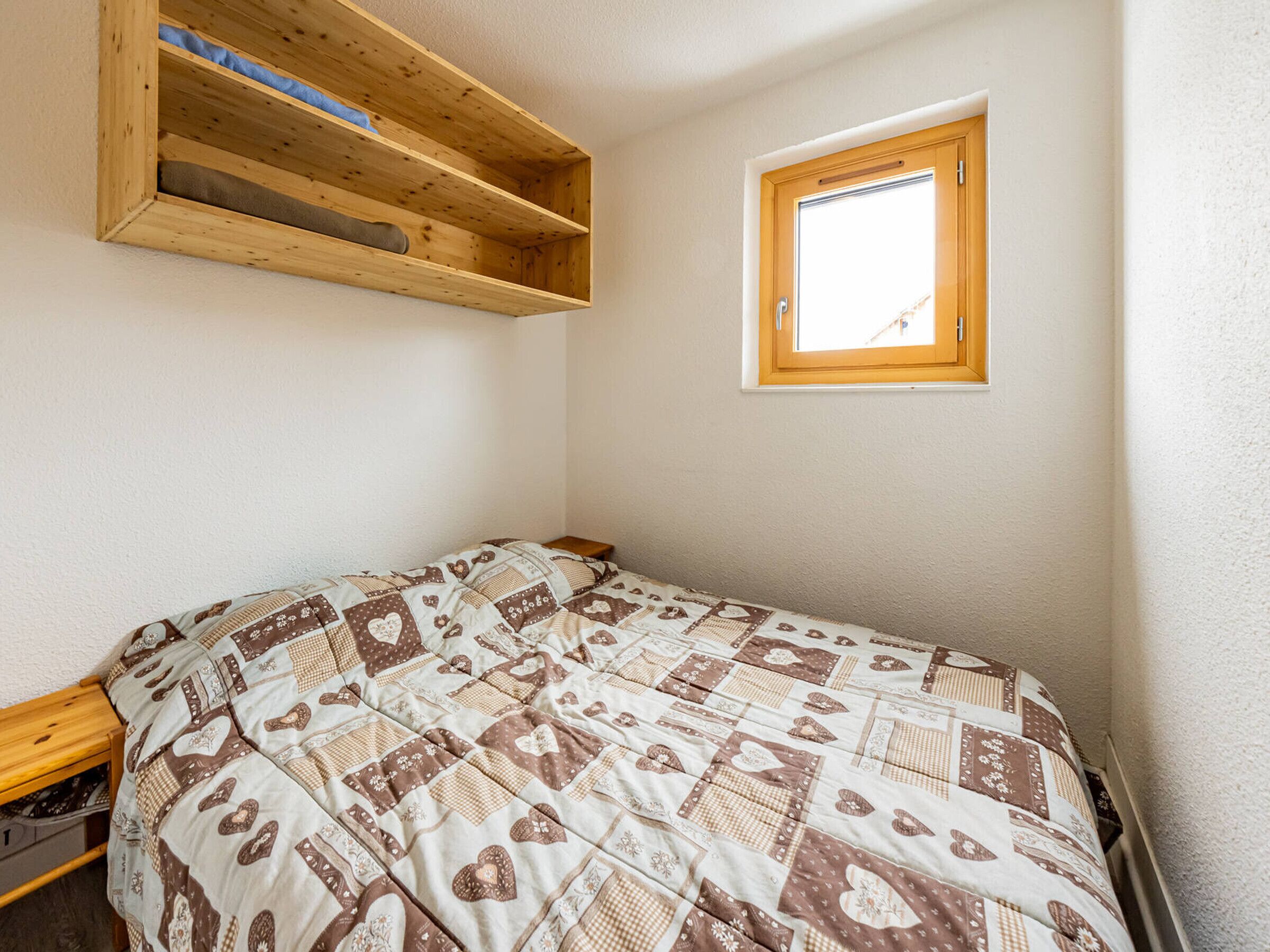 A bedroom with a bed, a wooden shelf, and a window.