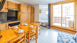 Een knus ingerichte kamer met houten meubels, een eettafel met kopjes en schotels, een bank en een balkon met uitzicht op gebouwen.