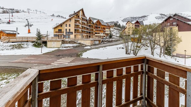 Een bergresort bedekt met sneeuw, met meerlaags gebouwen, een skilift en een houten brug.