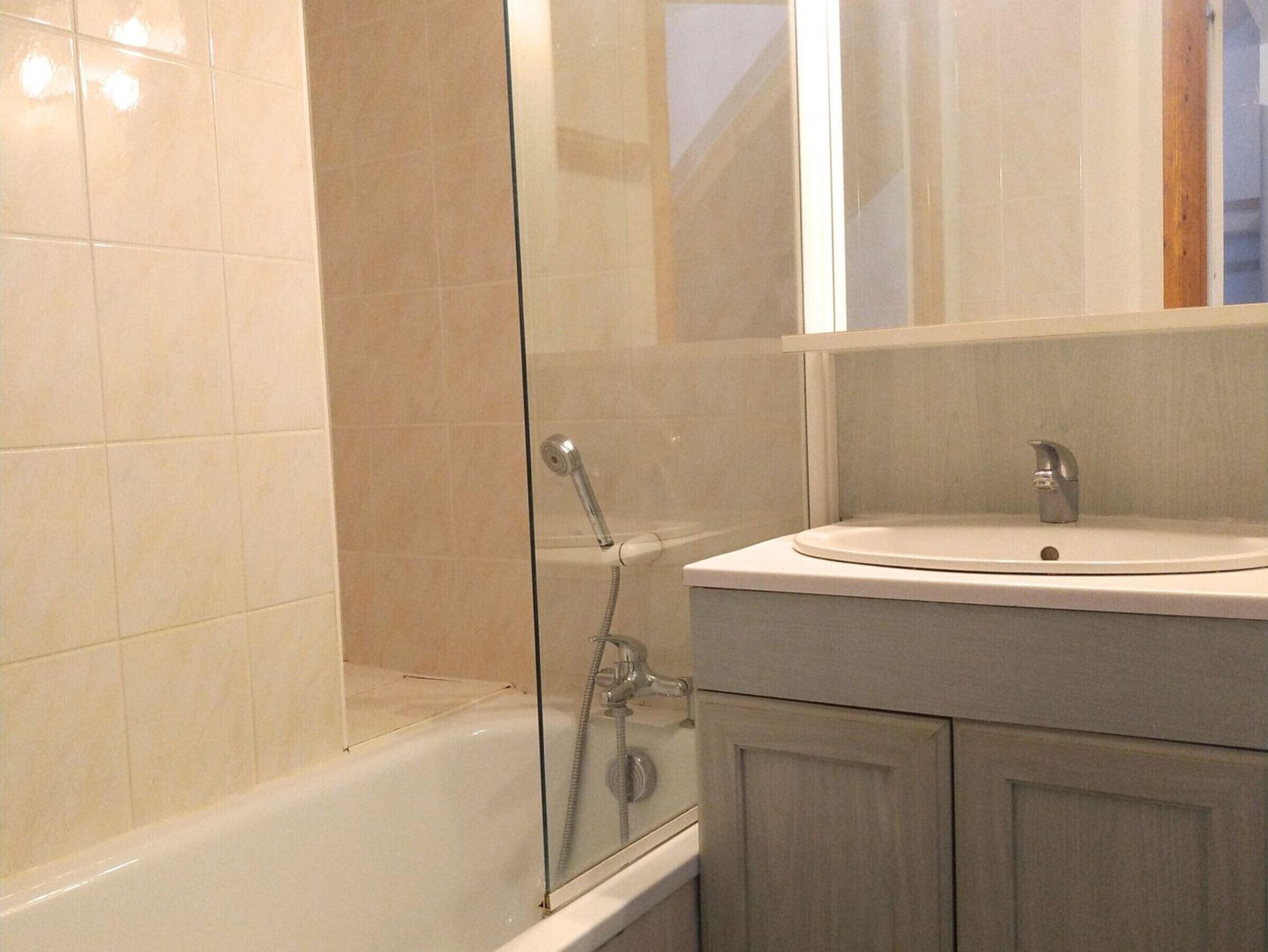 A bathroom with a glass-enclosed shower, a white sink, and wooden cabinets.