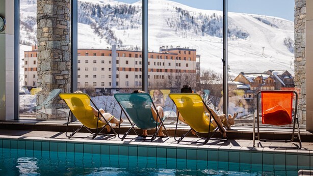 A poolside area with lounge chairs and a view of a snowy mountain and buildings. - Modern 25m² studio for 4, at the foot of the slopes (Saint-François-Longchamp)