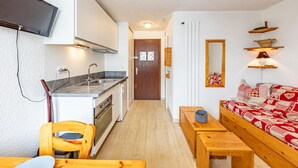 Una cocina compacta con electrodomésticos modernos, un comedor con una mesa y sillas de madera, y una sala de estar acogedora con un sofá y una manta estampada.