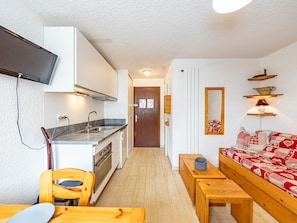 A compact kitchen with modern appliances, a dining area with a wooden table and chairs, and a cozy living space with a sofa and a patterned throw blanket. - Charming 19m² studio for 4 in Saint-François-Longchamp (Saint-François-Longchamp)