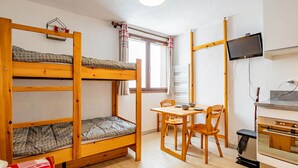 Un dormitorio con literas, una mesa de comedor con sillas, un televisor montado en la pared y una pequeña cocina.