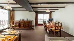 A cozy living room with a wooden dining table, chairs, a sofa, and a cabinet. There is a balcony visible through the window. - 8-person apt at the slopes, south-facing balcony, central location (Saint-François-Longchamp)