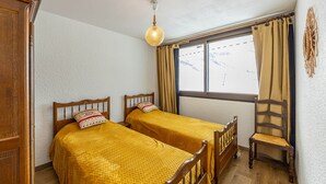 A room with two wooden beds, a wooden chair, a window with curtains, and a hanging light fixture. - 8-person apt at the slopes, south-facing balcony, central location (Saint-François-Longchamp)