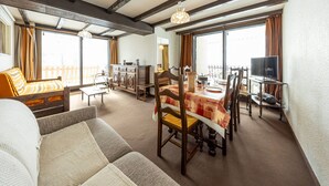 A spacious living area with a dining table, wooden chairs, a sofa, and a television. - 8-person apt at the slopes, south-facing balcony, central location (Saint-François-Longchamp)