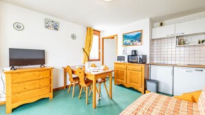Une pièce de taille modeste comprenant un lit, un téléviseur, une table à manger avec des chaises, un coin cuisine avec un four à micro-ondes et un petit réfrigérateur.