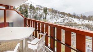 Un balcon avec une table et des chaises, donnant sur un paysage enneigé, avec des arbres et une montagne à l’horizon.