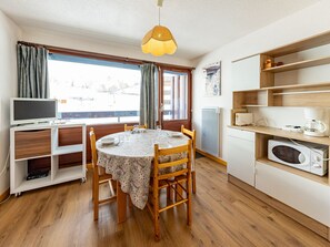 Uma cozinha compacta com mesa de jantar, cadeiras de madeira, televisão e frigorífico.