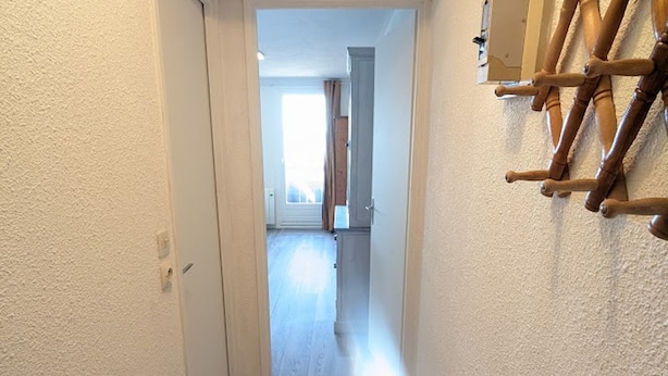 Un couloir doté d’un plancher en bois, d’une porte blanche et d’une étagère en bois fixée au mur.