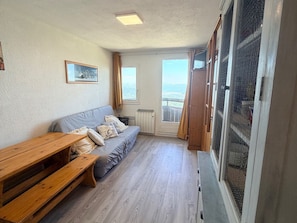 Quarto com sofá, um banco de madeira, janela com cortinas e porta para área externa.