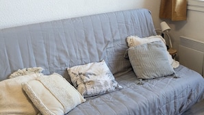 Un canapé gris recouvert de tissu, agrémenté de trois coussins, une lampe et un radiateur, dans une pièce aux murs blancs.
