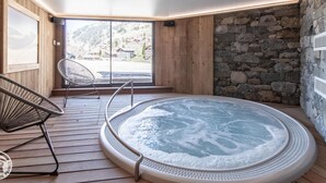 Ein Whirlpool in einem Holzraum mit einer Steinwand und Blick auf eine verschneite Landschaft.