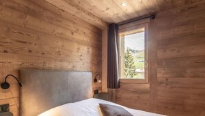 Ein Schlafzimmer einer Holzhütte mit einem Bett, Kissen, einem Nachttisch, einer Lampe und einem Fenster mit Blick ins Freie.