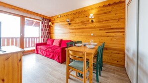 Un interior de madera con una mesa de comedor para cuatro personas, un sofá rojo y un balcón con barandilla.