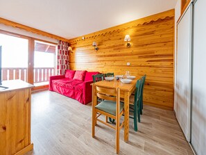 Ein Holzinnenraum mit einem für vier Personen gedeckten Esstisch, einem roten Sofa und einem Balkon mit Geländer.