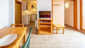 Un espacio habitable compacto con comedor, kitchenette y televisor sobre un soporte de madera.