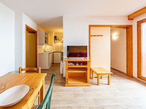 Ein kompakter Wohnbereich mit Essbereich, Küchenzeile und Fernseher auf einem Holzgestell.
