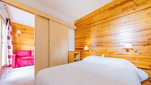 Un dormitorio con pared de madera, una cama, una mesita de noche y una silla roja.