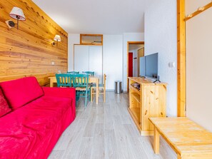 Ein gemütlicher Wohnraum mit einem roten Sofa, blaugrünen Sesseln, einem Holztisch und einem Fernseher auf einem Holzschrank.