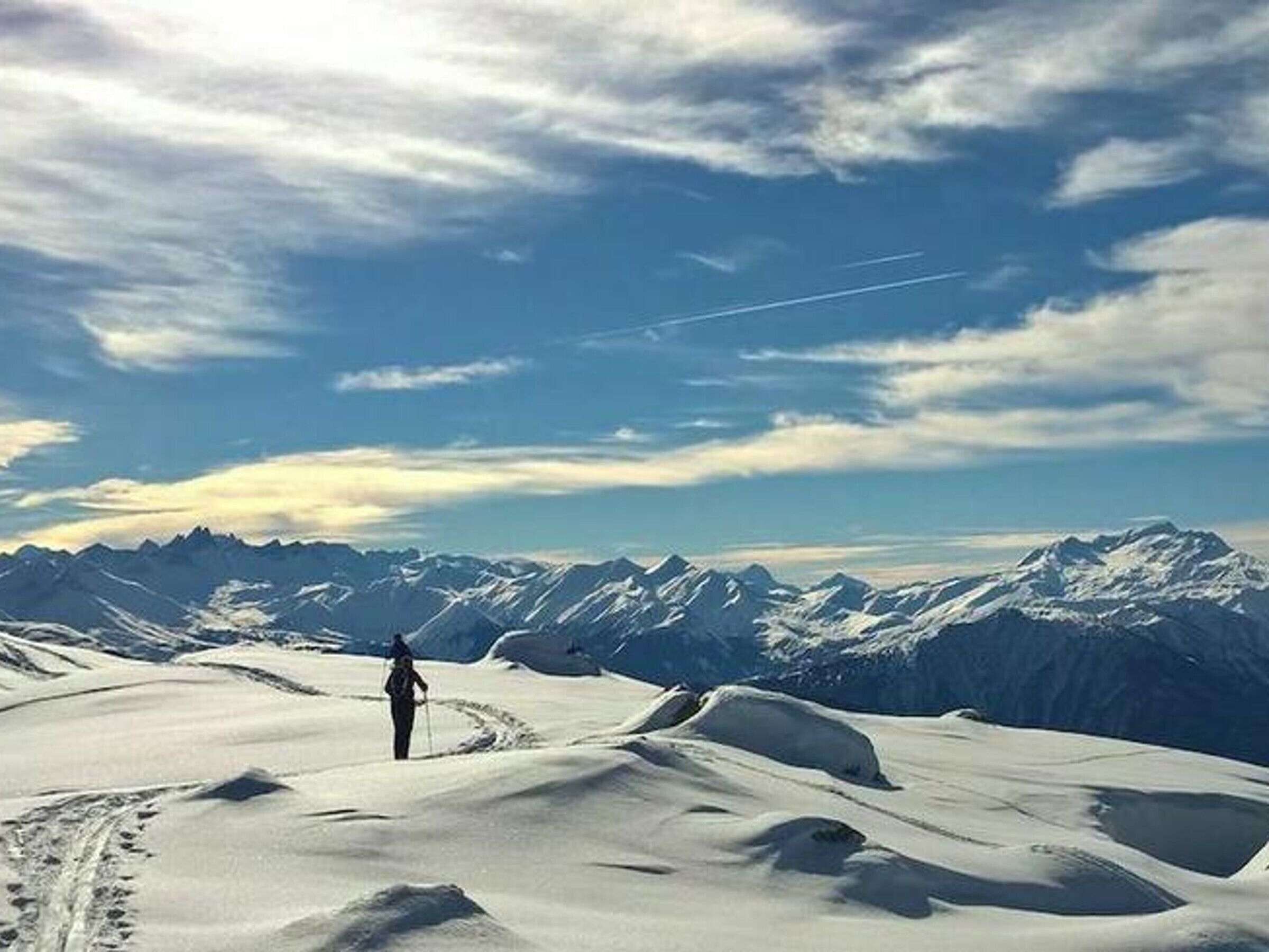 A snowy landscape with a person walking on a snow-covered path, surrounded by mountains and a clear sky.