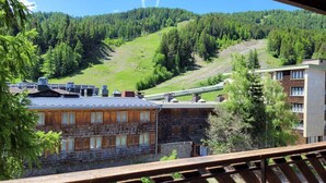 A view from a balcony overlooking a mountainous area with a wooden building and a modern structure. - 3 rooms for 6, south/east balcony near slopes (Pra-Loup)