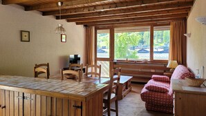 A cozy room with a wooden dining table, chairs, a bench, and a window with a view of buildings and trees. - 3 rooms for 6, south/east balcony near slopes (Pra-Loup)