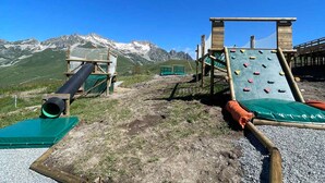Un parque infantil con estructuras para escalar y un tobogán, con montañas al fondo.