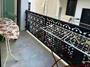 A balcony with a patterned metal railing, a table with a floral tablecloth, and a chair.