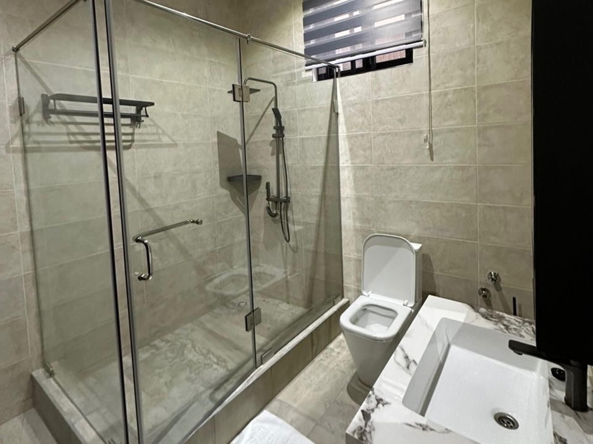 A modern bathroom with a glass-enclosed shower, a toilet, and a sink with a marble countertop.