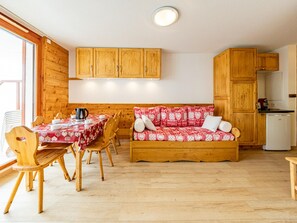 A cozy room with wooden walls and furniture, a dining table with chairs, a sofa, and a small kitchen area.