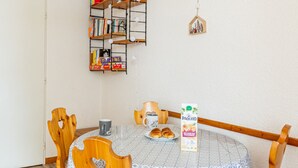 Una mesa redonda de madera con mantel estampado, rodeada de sillas de madera con corte en forma de corazón. Hay un cartón de jugo Paquito sobre la mesa.