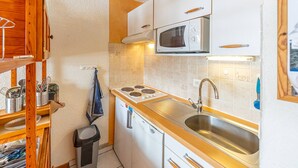 Cocina compacta con alacenas blancas, microondas, fregadero y estufa.