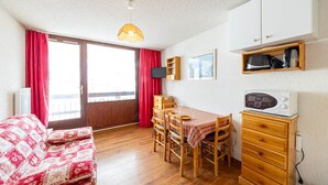 A cozy room with a wooden dining table, chairs, a red and white checkered tablecloth, a microwave, and a wooden cabinet.