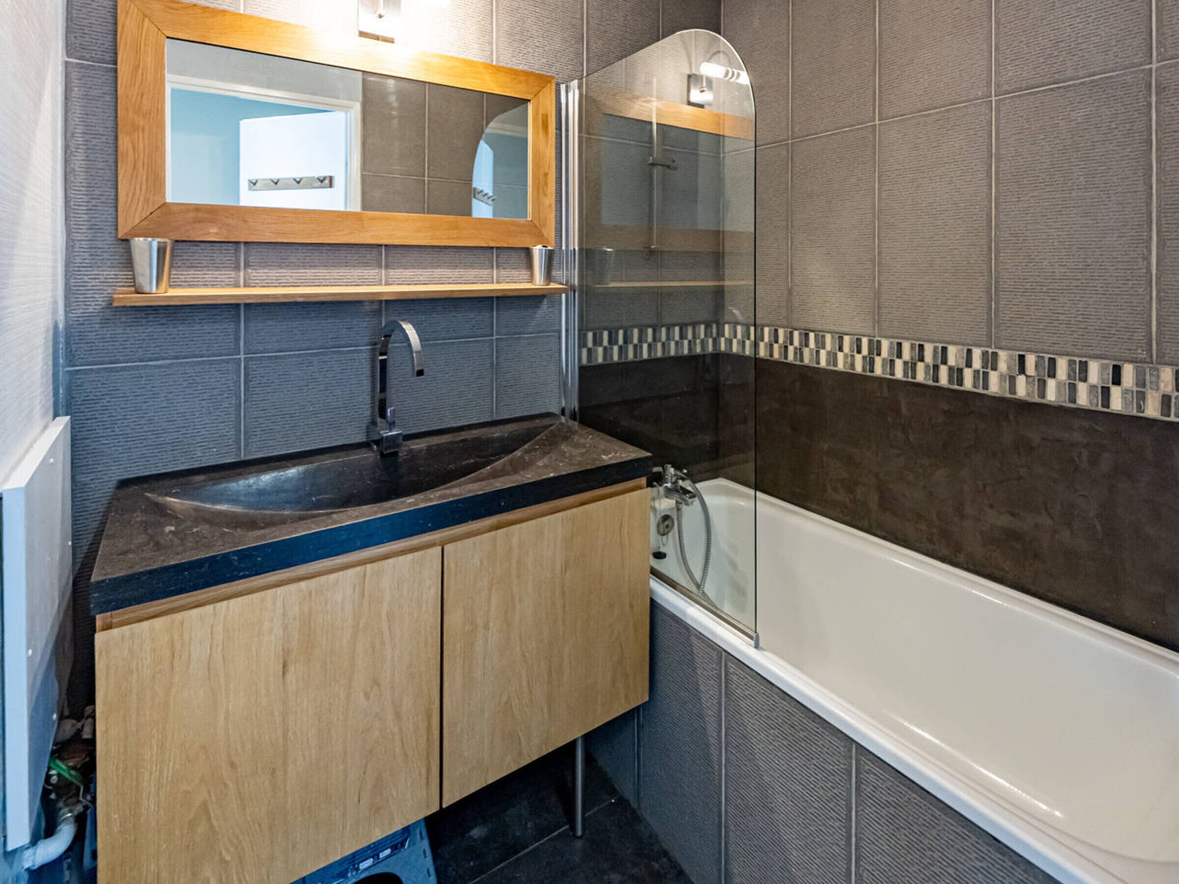 Ein modernes Badezimmer mit einem Holzkonsolenbecken, einem Waschbecken, einem Spiegel und einer Badewanne.