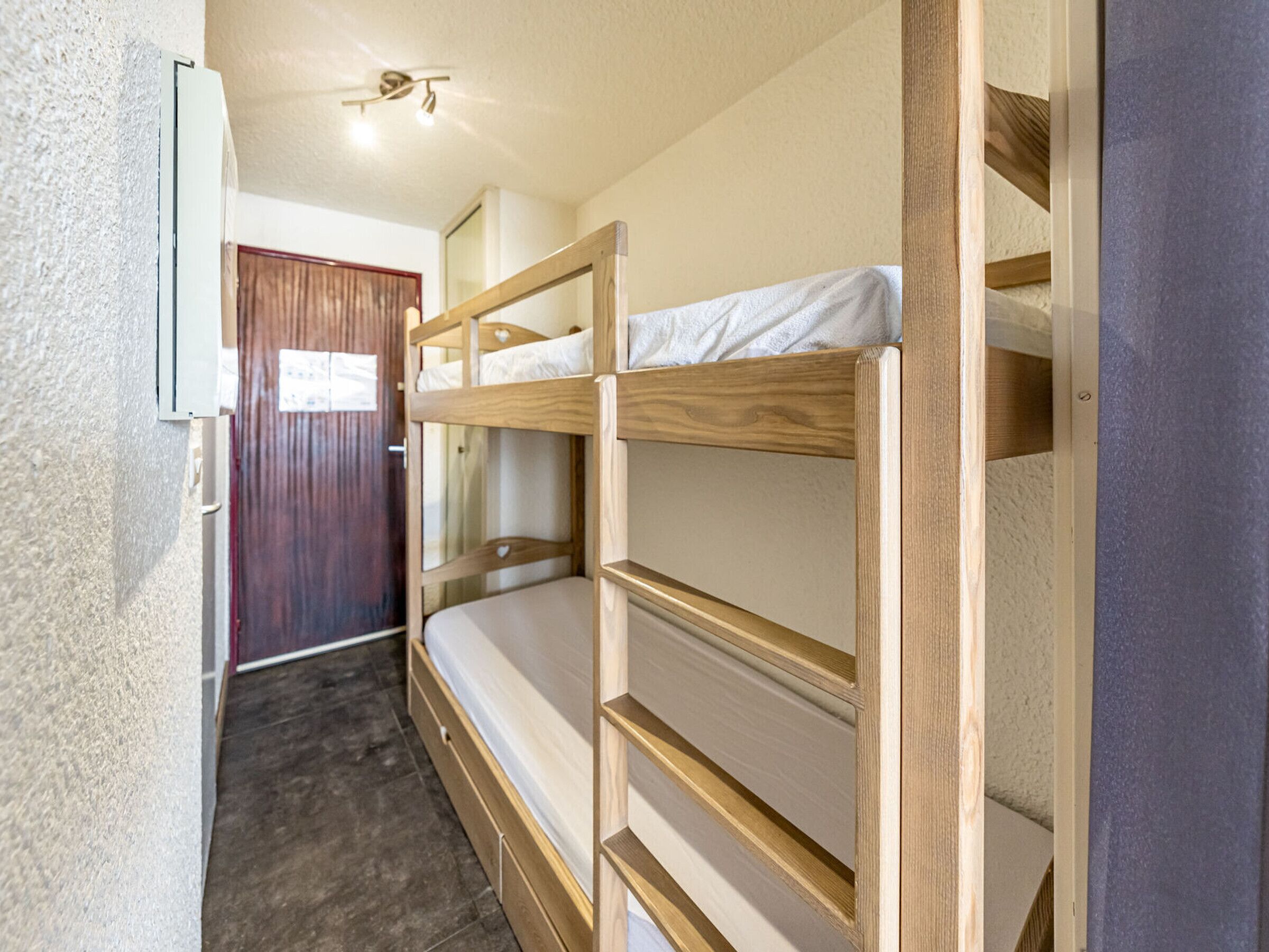 Une chambre avec un lit superposé, une tête de lit en bois, une porte et un ventilateur de plafond.