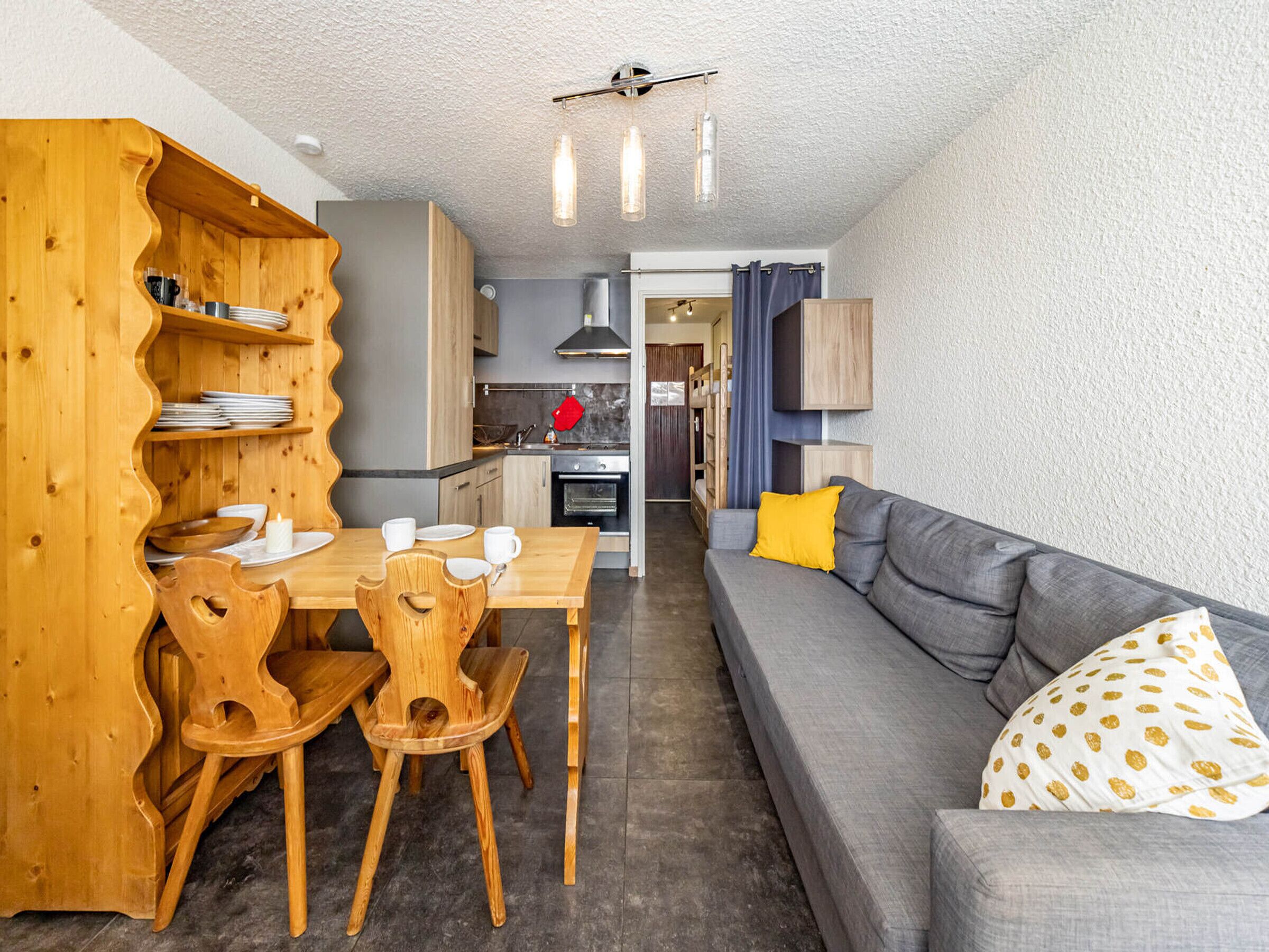 Un espacio habitable compacto con comedor, kitchenette y un sofá con cojín estampado.