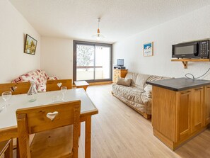 A cozy living room with a wooden dining table, a sofa, and a kitchen area with a microwave. - Comfortable studio at ski lift base, south balcony (Saint-François-Longchamp)