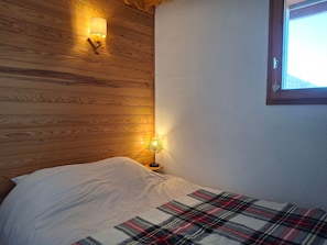 A bedroom with a wooden headboard, a bedside lamp, a plaid blanket, and a window with daylight. - 6-person apartment on the slopes in St-François-Longchamp (Saint-François-Longchamp)