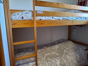 Een stapelbed met een houten frame, een onderste bed met een geborduurd kleed en een hoofdbord met een etiket.