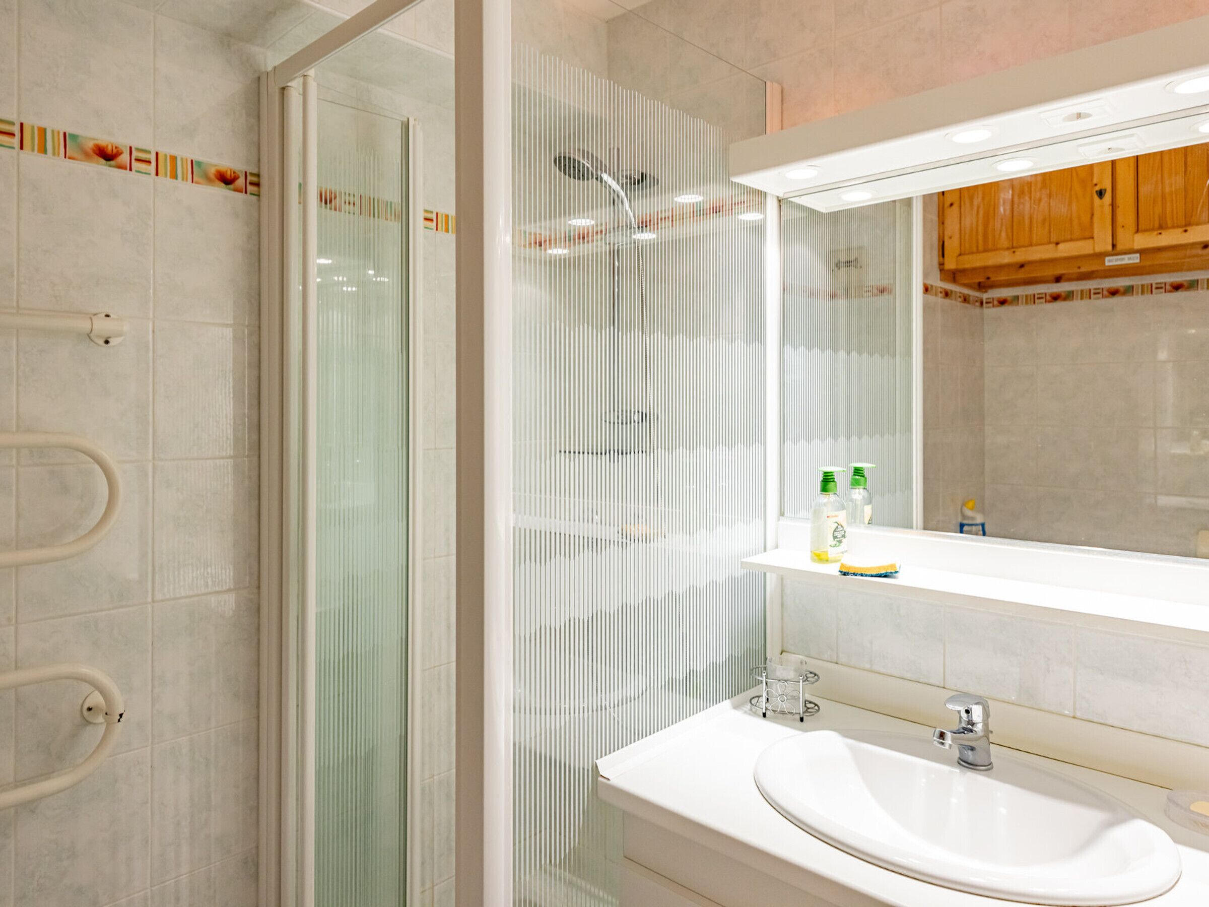 A modern bathroom with a glass shower enclosure, a white sink, and a mirror above it.