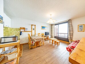 Una sala de estar acogedora con comedor, muebles de madera, una cocina con tostadora y un ventanal con cortinas.