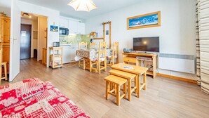 A cozy living room with a wooden table, chairs, a TV, and a kitchen in the background.