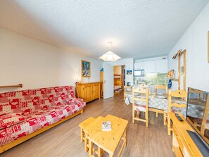 Una sala de estar acogedora con un sofá estampado en rojo y blanco, una mesa de comedor de madera y una zona de cocina con microondas y fregadero.